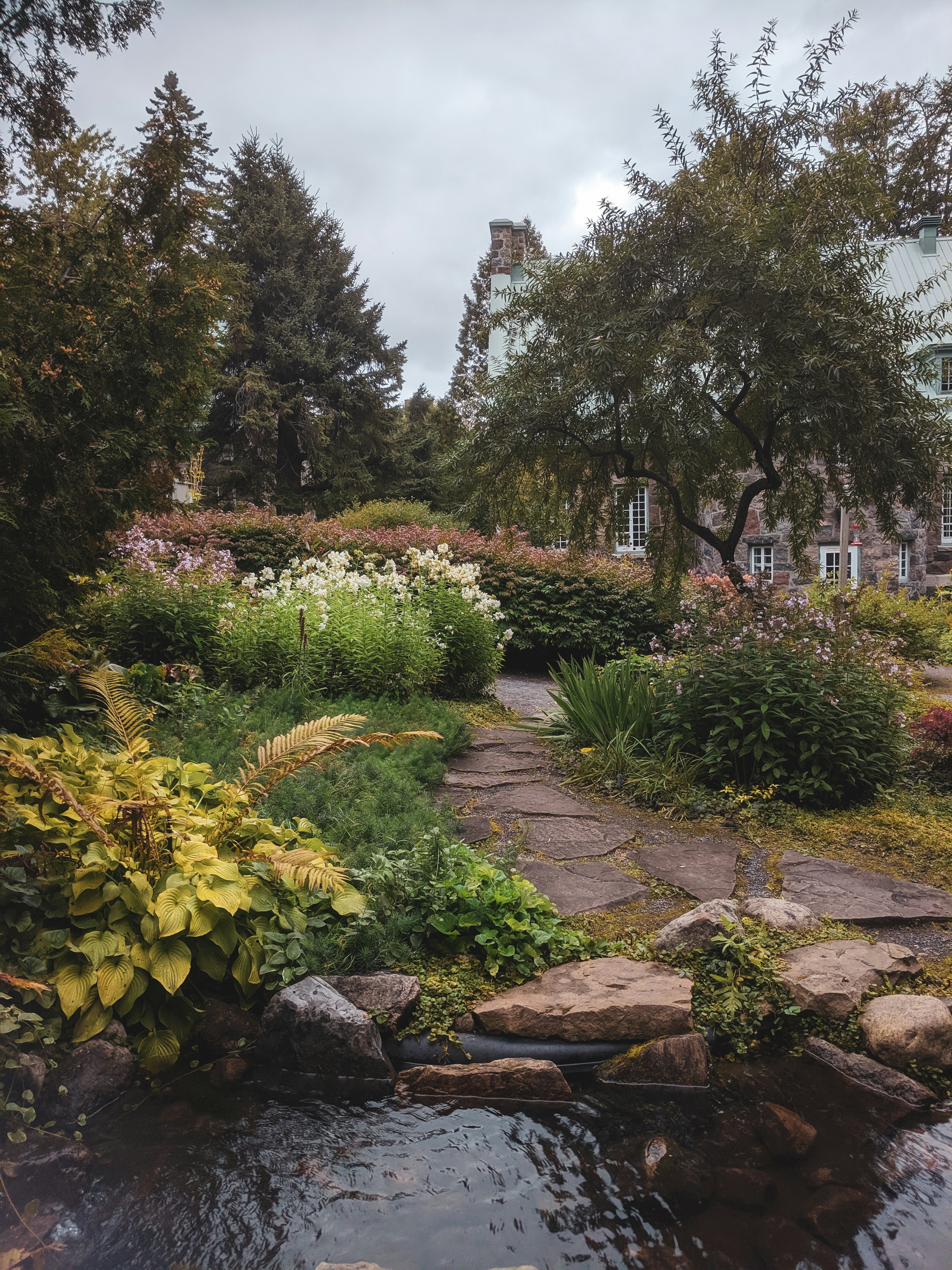 Professionell gestalteter Garten mit Natursteinweg, üppiger Bepflanzung und Wasserelement - Beispiel für Gartenbau Hafner Projekte
